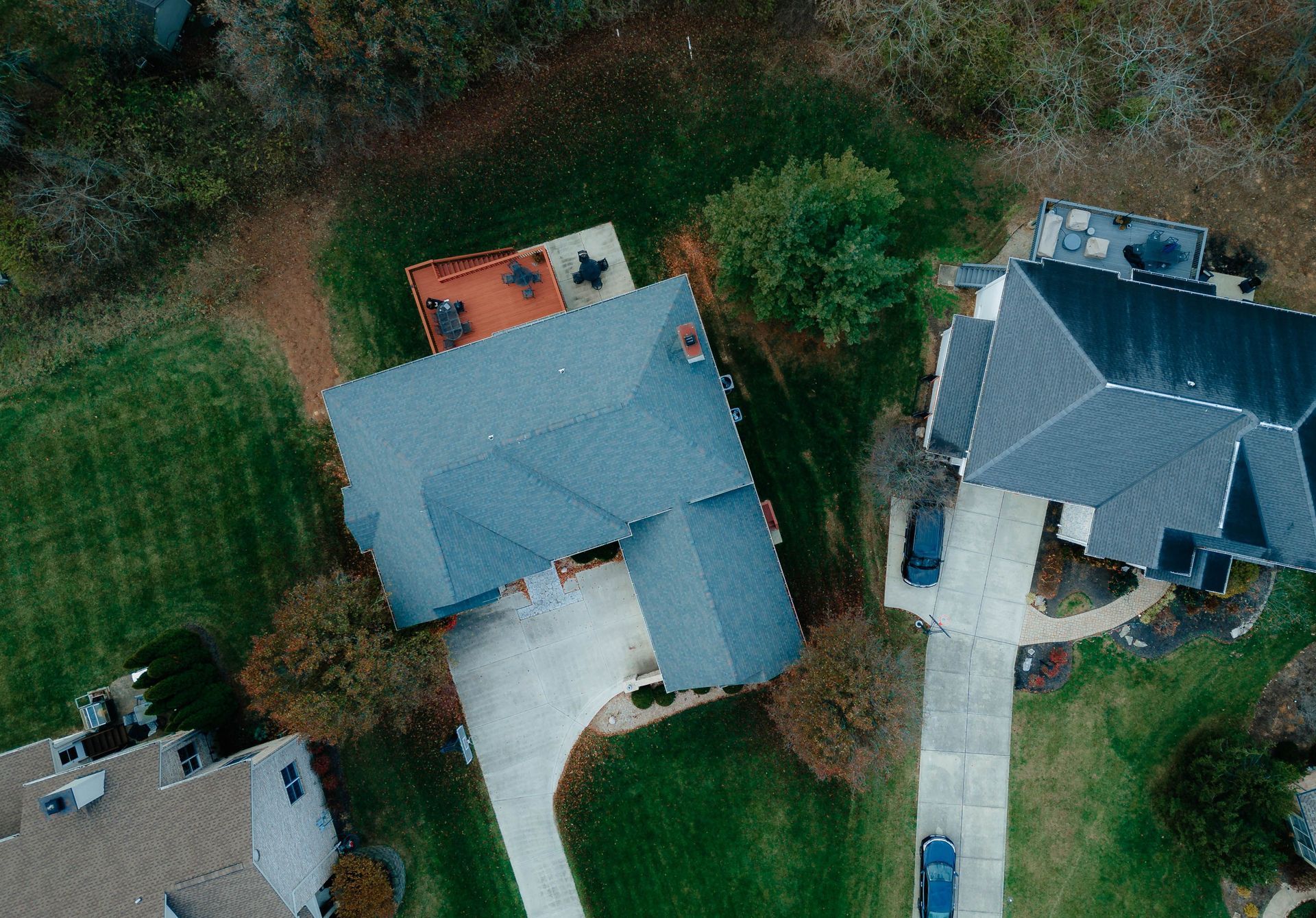 Aerial view of two houses with gray roofs, driveways, and surrounding trees.