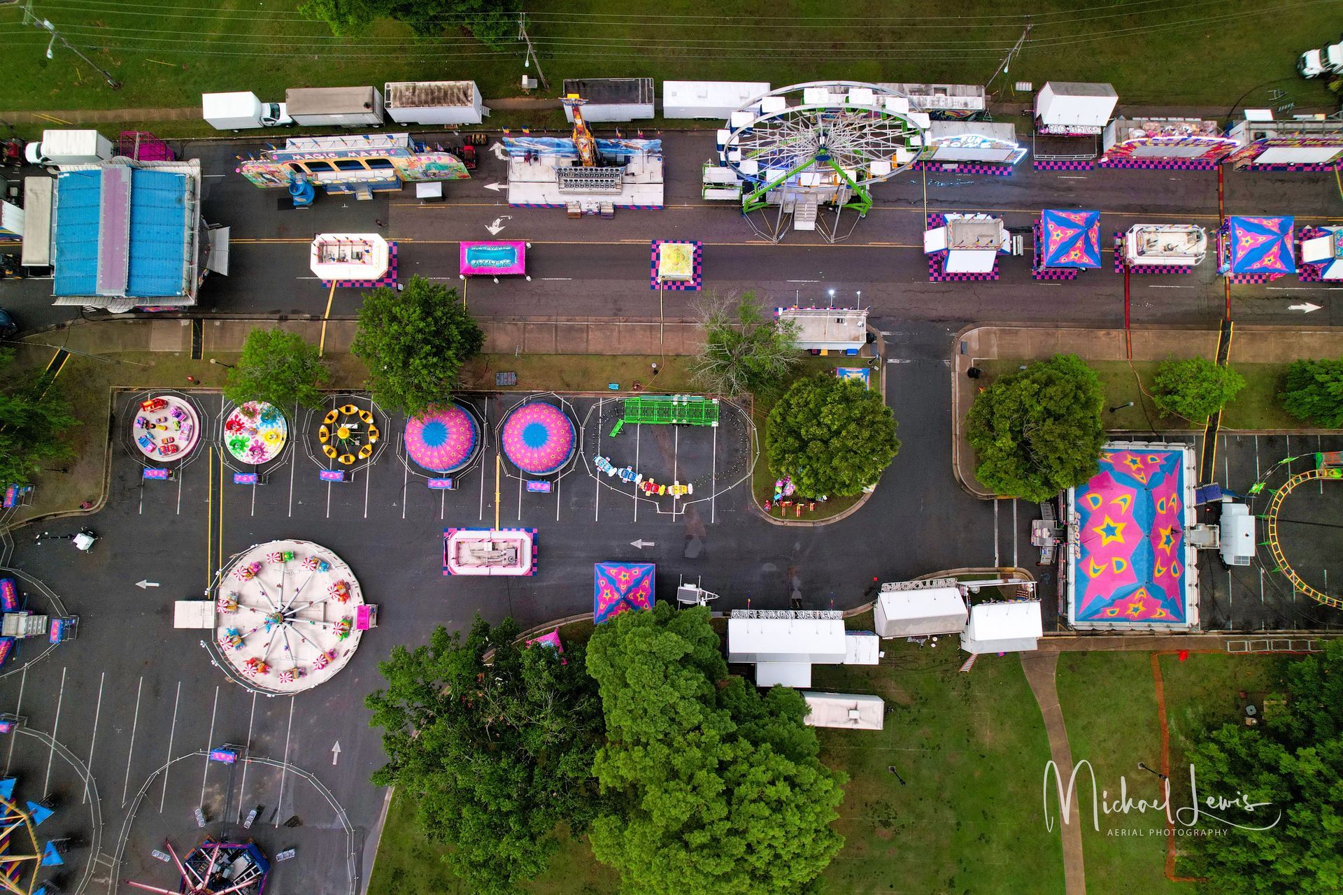 Aerial view of a colorful street festival with decorated booths, umbrellas, and people gathered along a road.