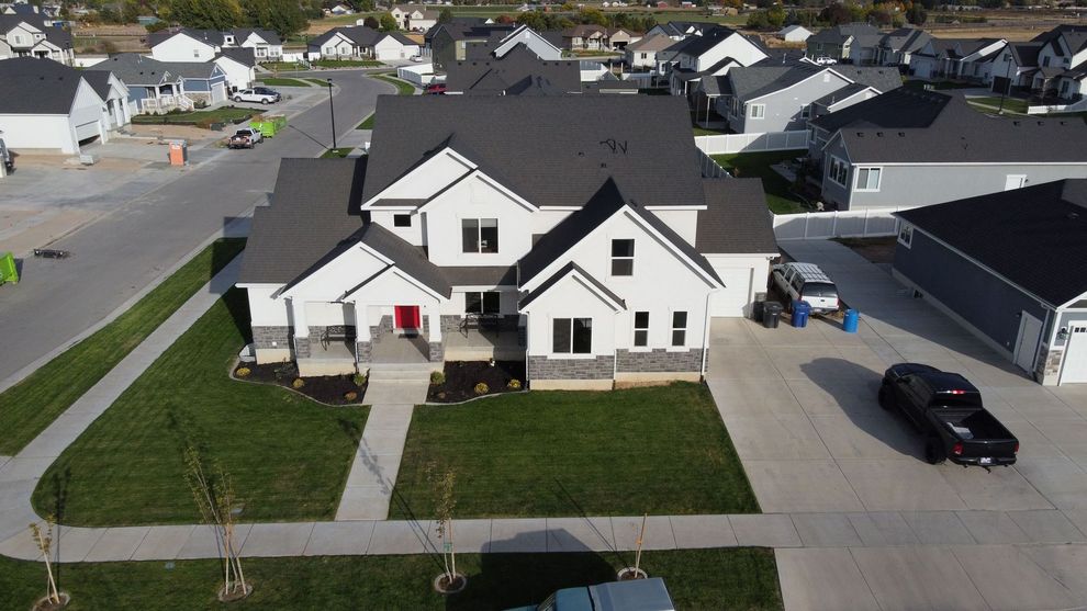 Aerial view of a white two-story house with a black roof, front lawn, driveway, and parked car in a suburban neighborhood