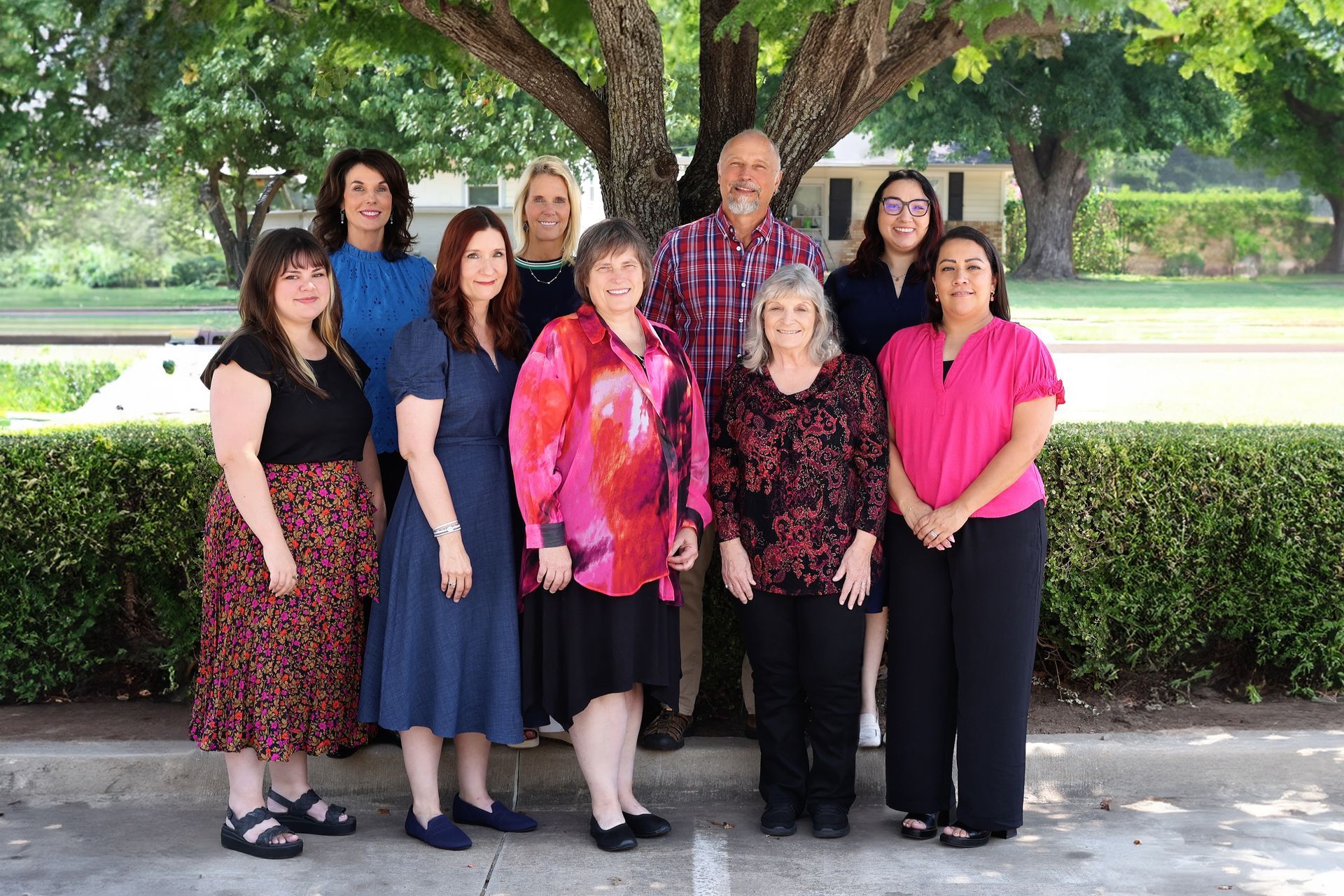 Group of people standing in front of a tree, smiling. Mostly women.