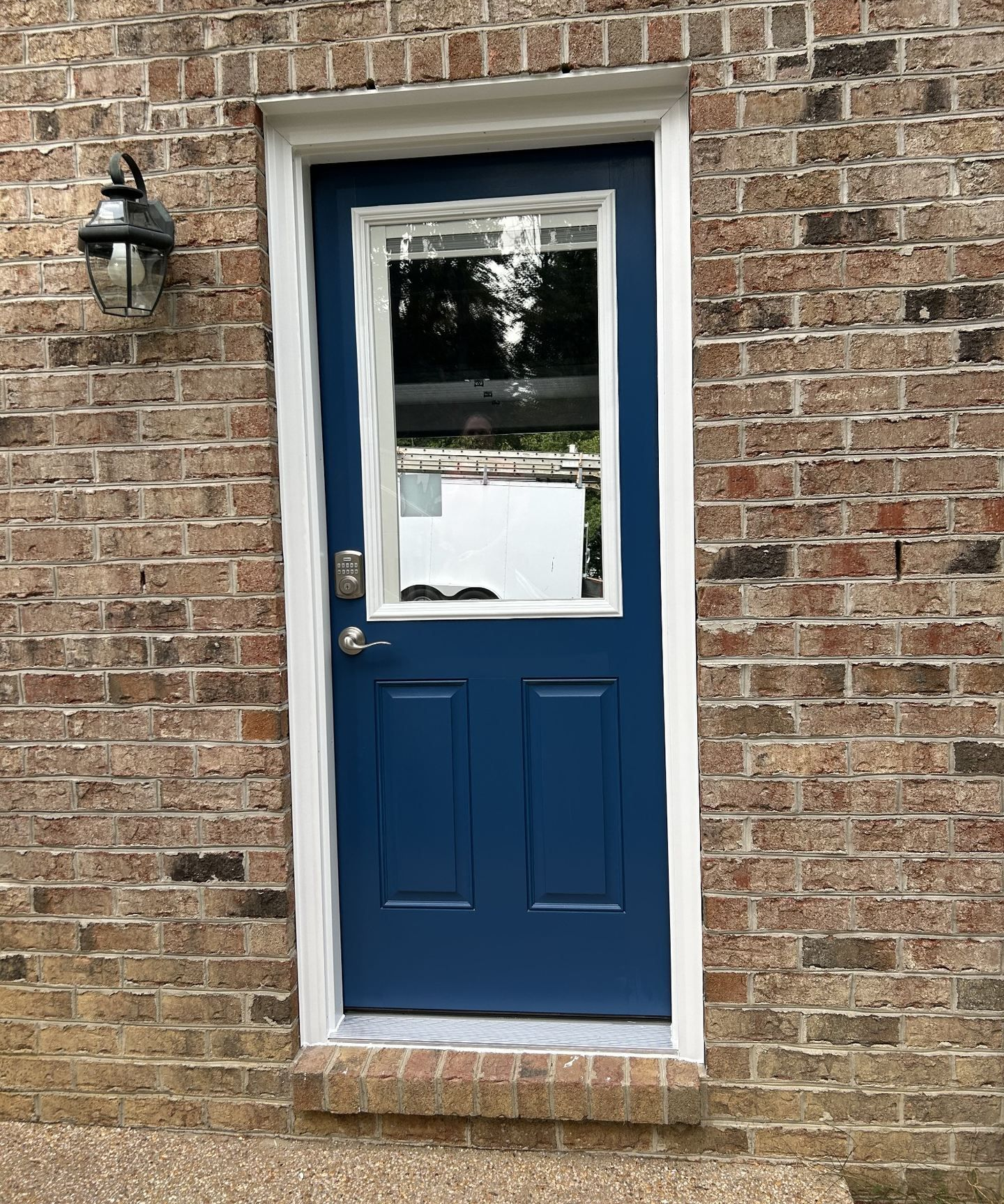 Blue exterior entry door with glass window, white trim, and keypad lock installed in a brick home.