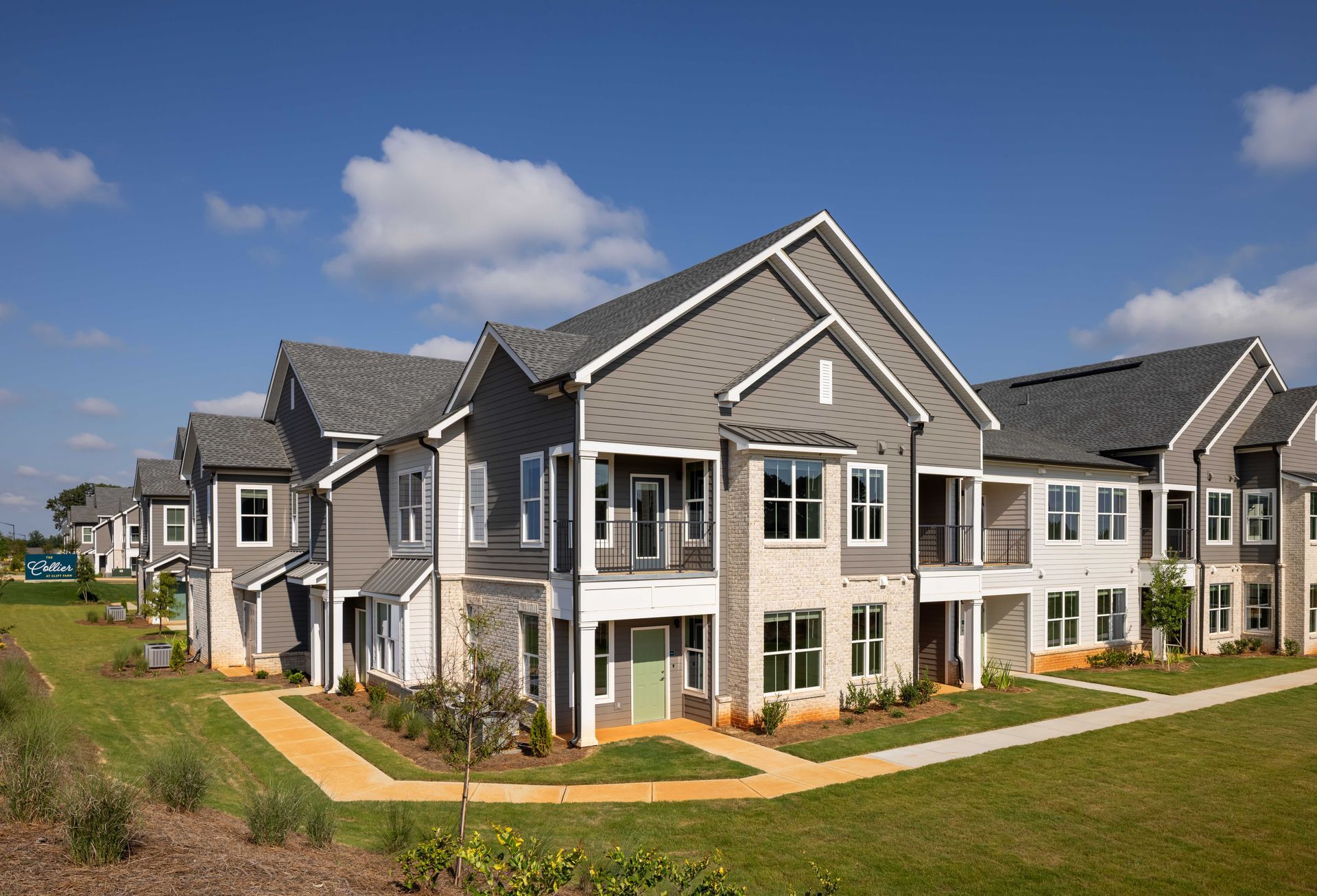 Apartment complex with gray siding, white trim, and green doors under a blue sky.