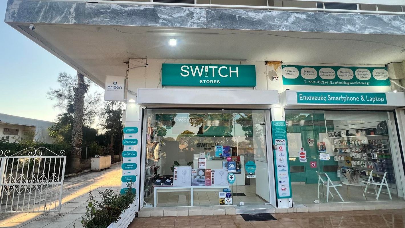 Εξωτερικό ενός καφέ SWITCH με πράσινη σήμανση και γυάλινη βιτρίνα κάτω από ένα στεγασμένο διάδρομο