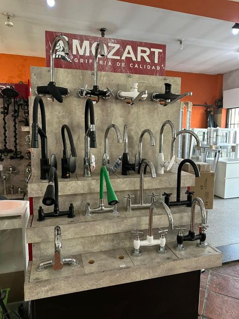 Exhibición de herrajes con grifos y accesorios de baño surtidos en estantes en una sala de exposición.
