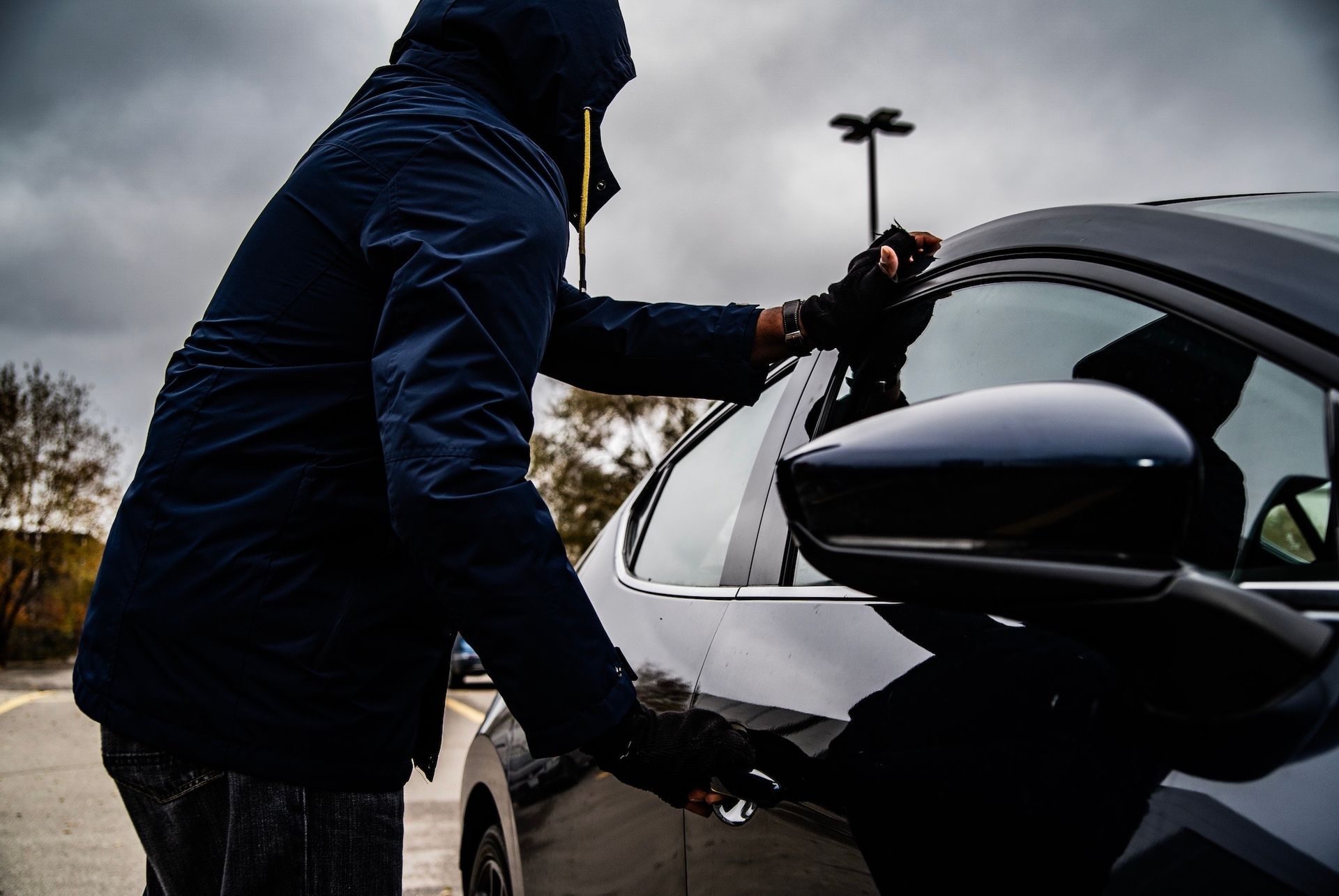 Person in dark clothing attempting to open a car door in a parking lot.