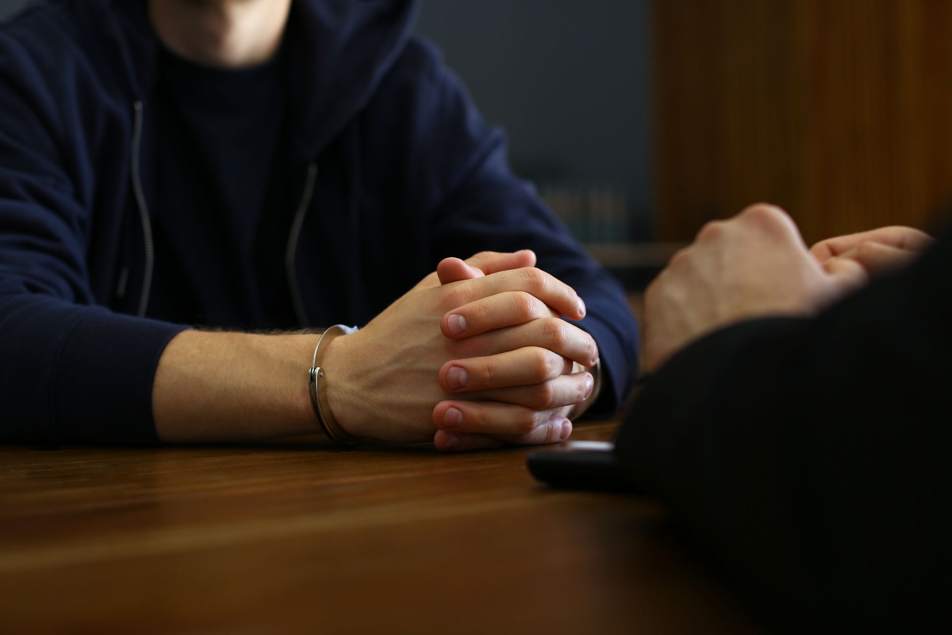 Person in handcuffs sits at a table, hands clasped, facing another person out of view.