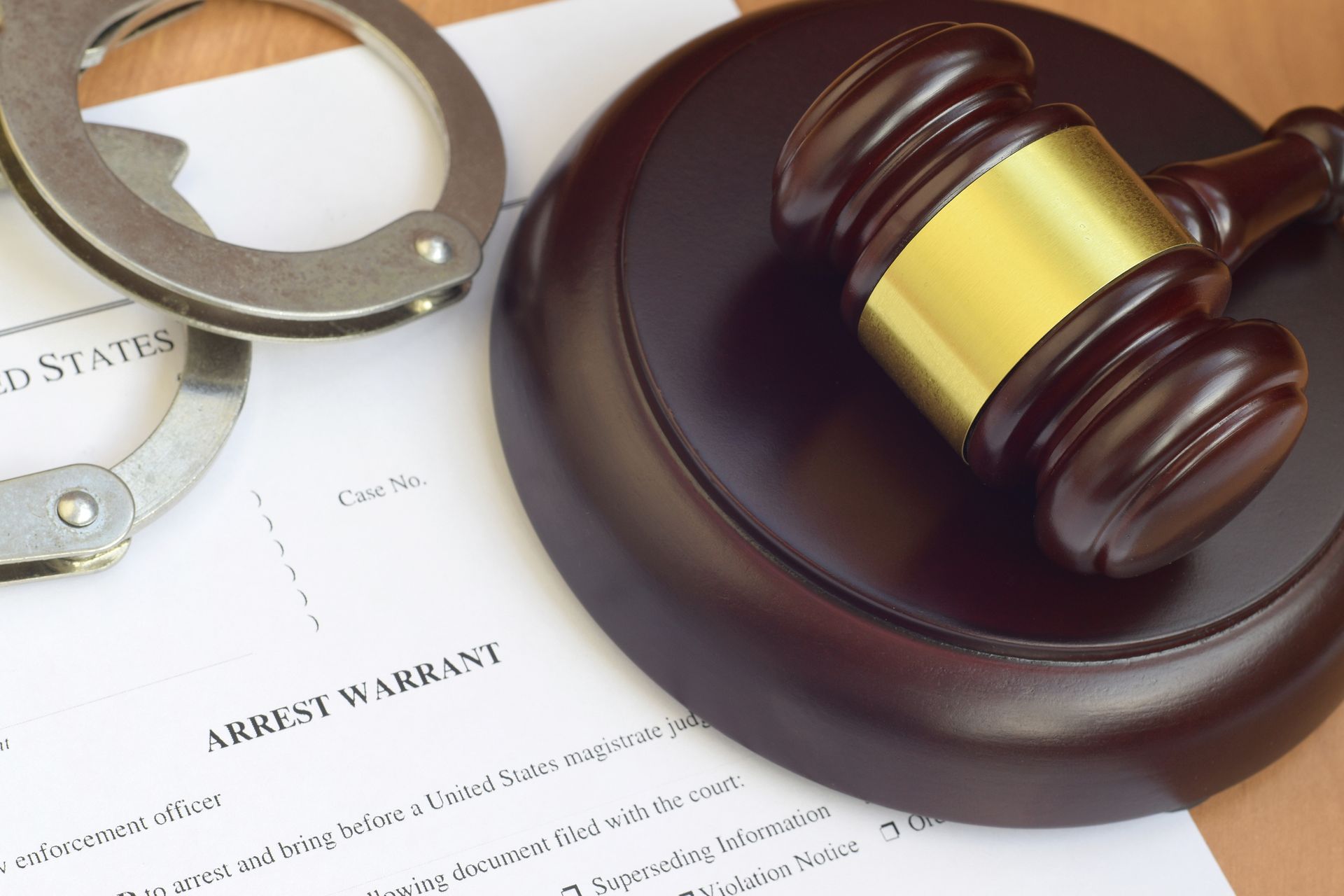 Handcuffs, gavel, and arrest warrant on a wooden surface, suggesting legal or law enforcement context.