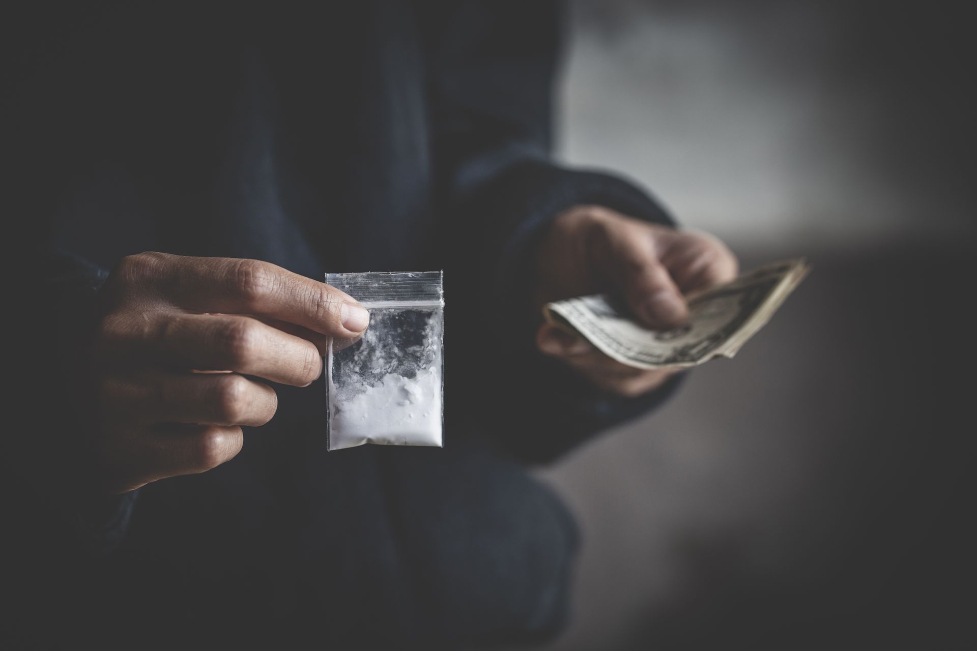 Hand holding a bag of white powder, receiving money.