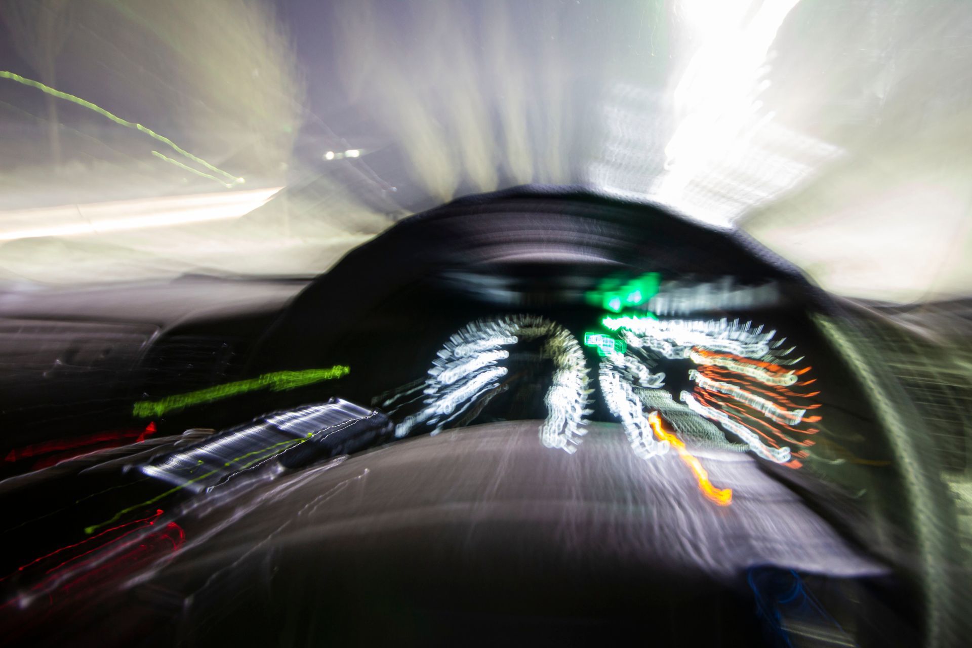 Blurred view from a car driving through a tunnel; lights streak, green and white colors.