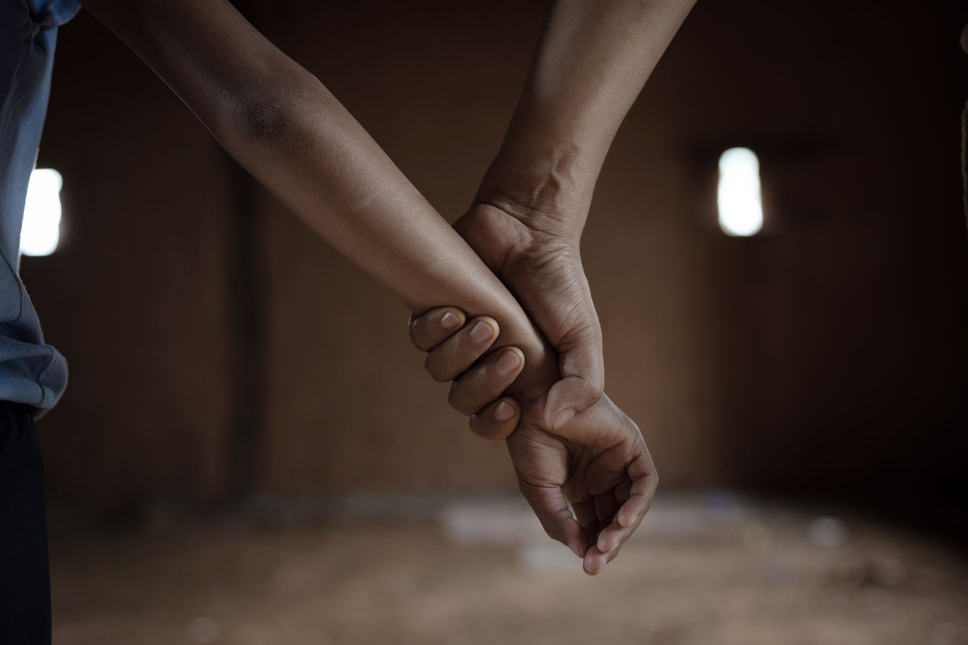 Two hands, one adult, one child, holding tightly in front of a dark, interior space.