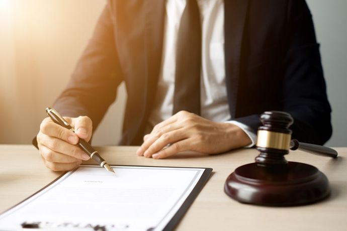 Person in suit signing a document, next to a gavel on a desk.