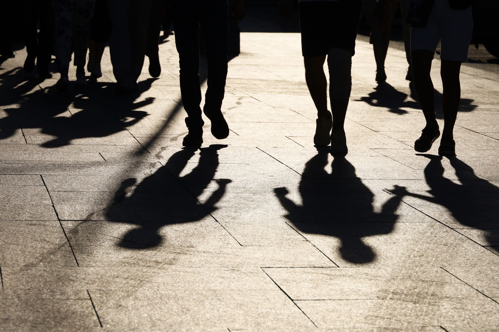 Silhouetted figures of people walking, casting shadows on a sunlit stone walkway.