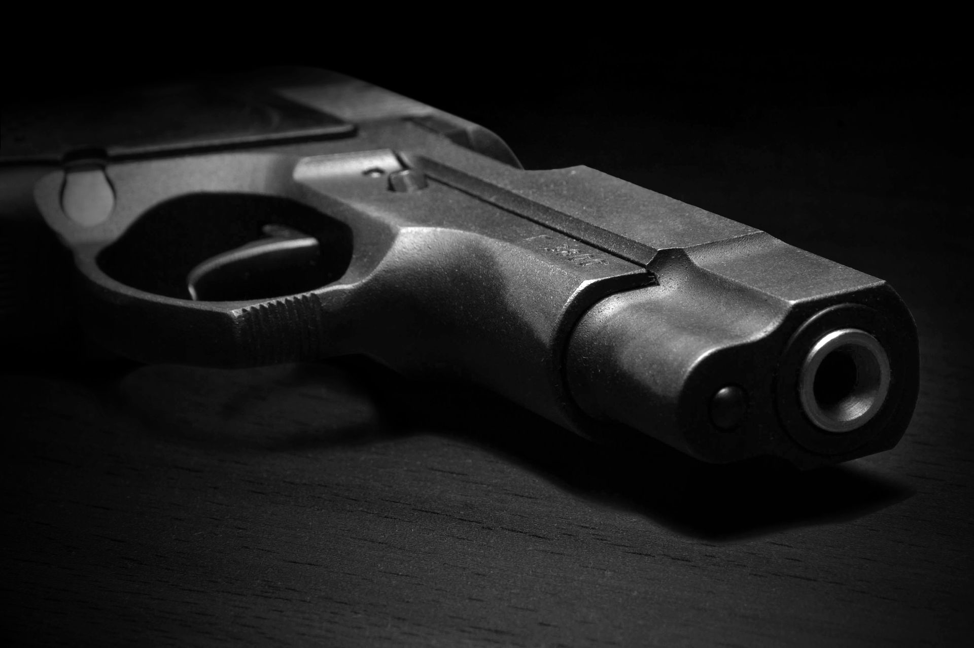 Black handgun on a dark surface, barrel pointed toward the viewer.