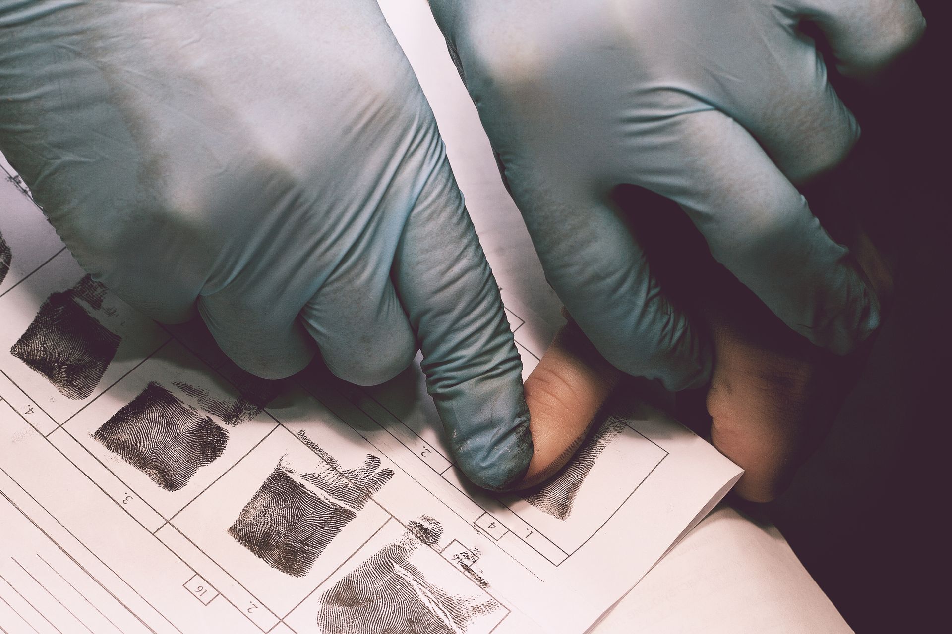 Hands in blue gloves taking fingerprints.