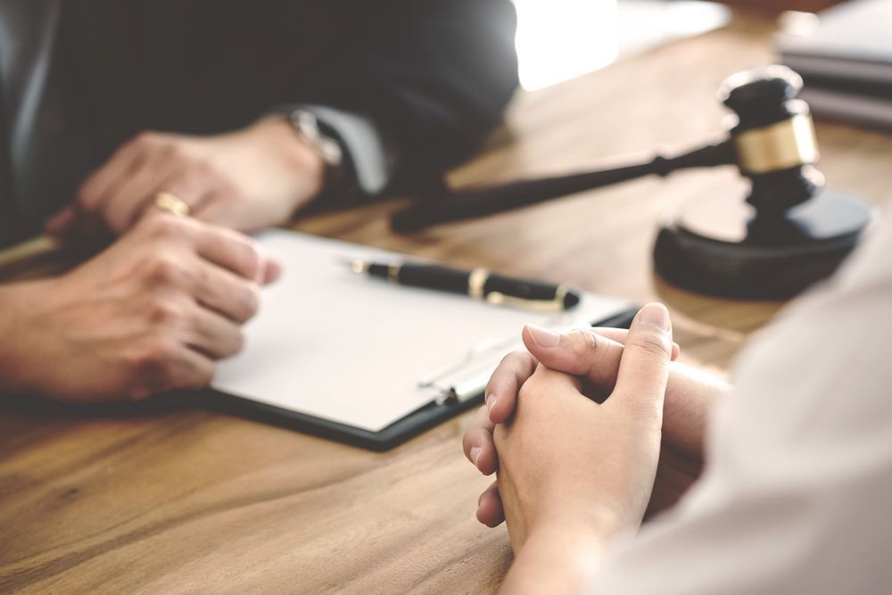 Hands clasped in a legal setting, next to a gavel and document, suggesting a consultation or testimony.