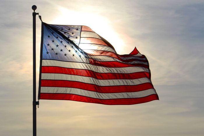 American flag waving on a flagpole against a cloudy sky at sunset