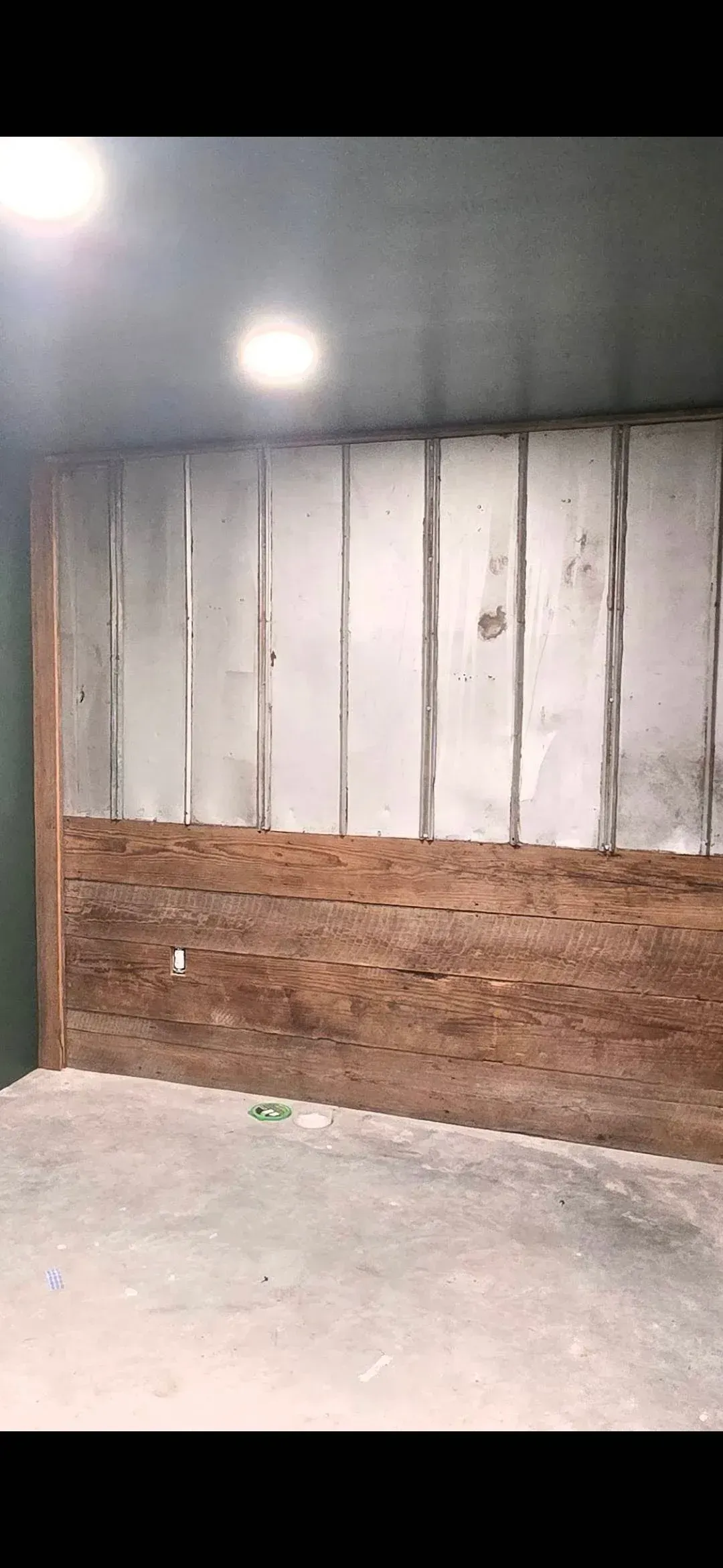 Empty indoor room with concrete floor, corrugated metal wall, and a single bright light overhead.