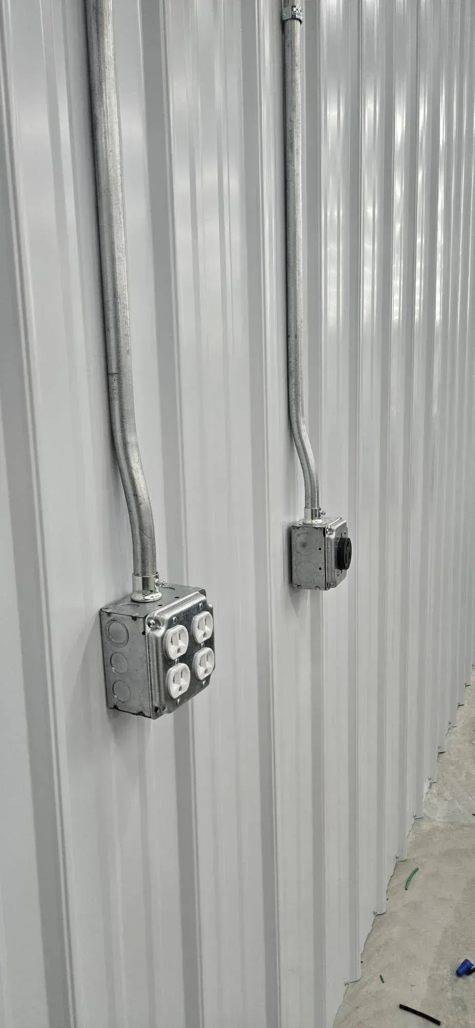 Two gray electrical junction boxes mounted on a corrugated metal wall with conduit running upward