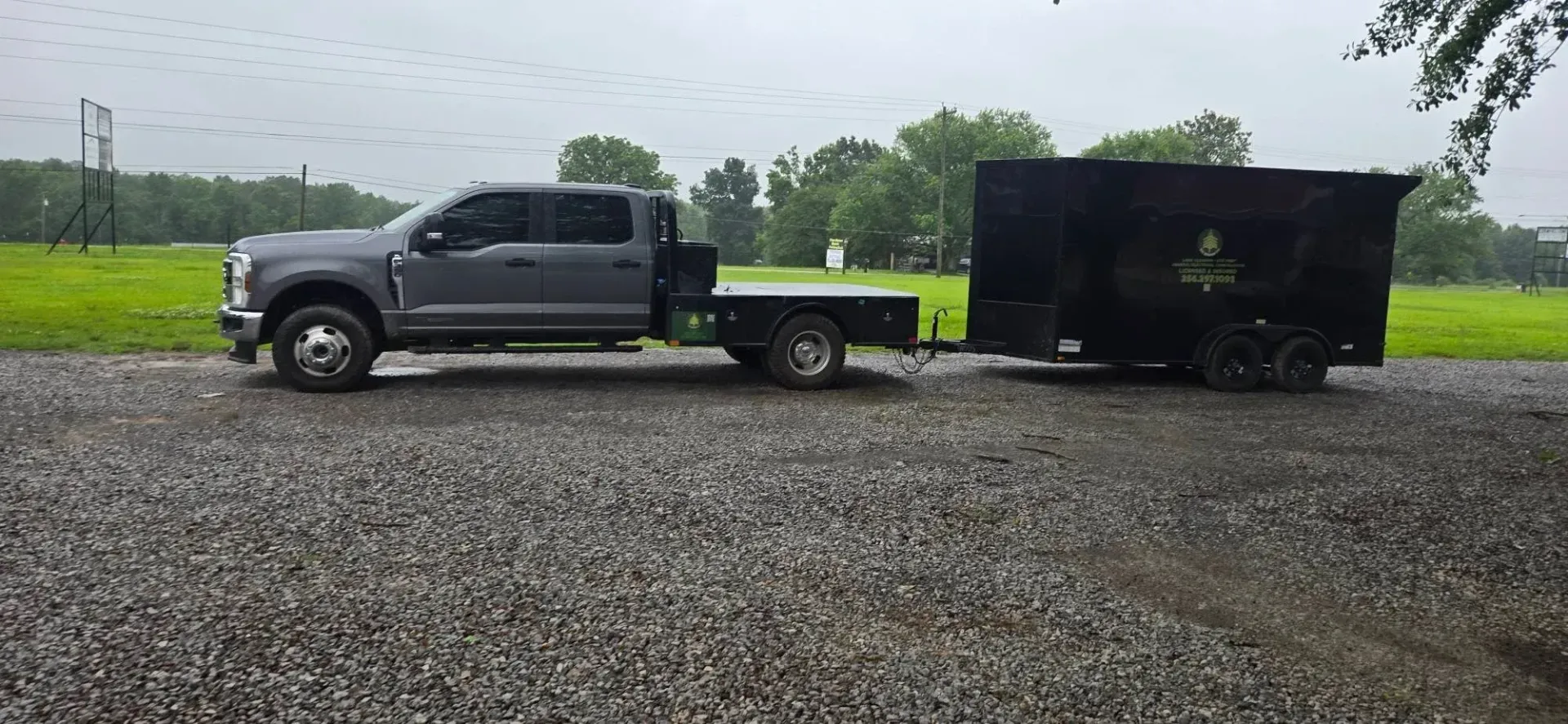 Gray pickup truck towing a black enclosed trailer on a gravel lot in the rain