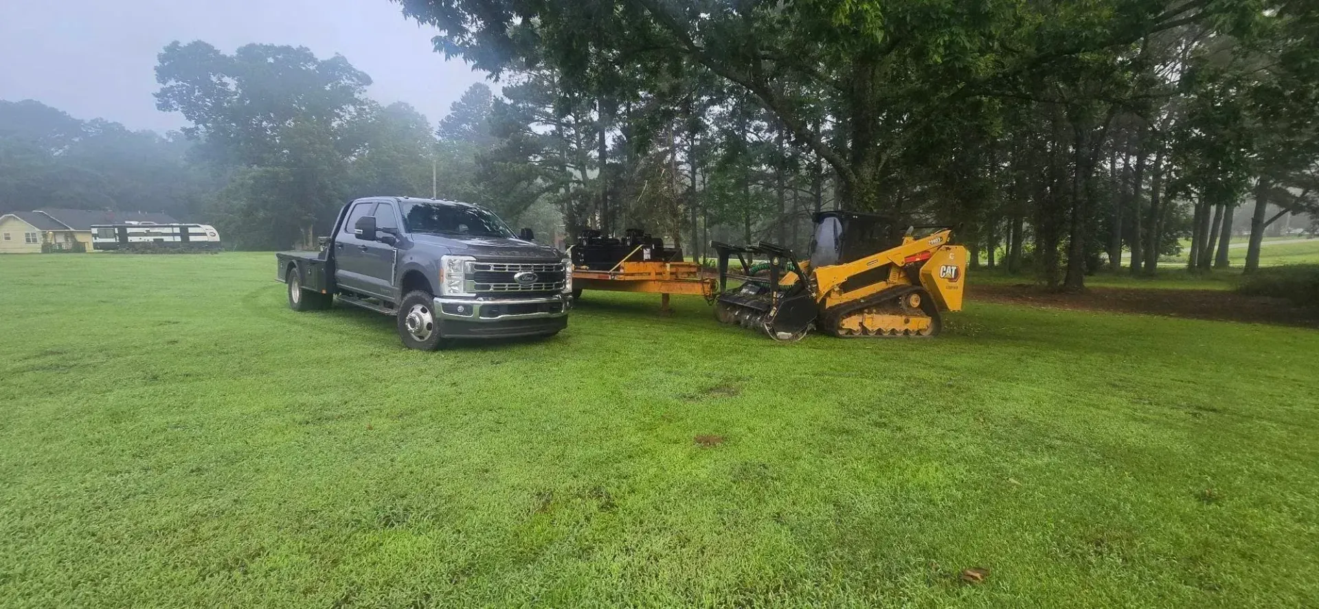 Pickup truck beside yellow excavator on a grassy field in light rain