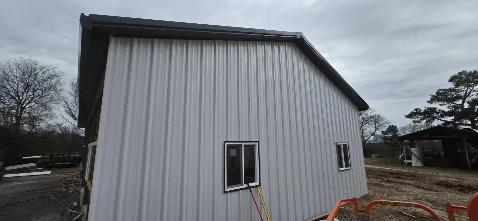 White-sided building under construction with a small window and exposed framing on a cloudy day