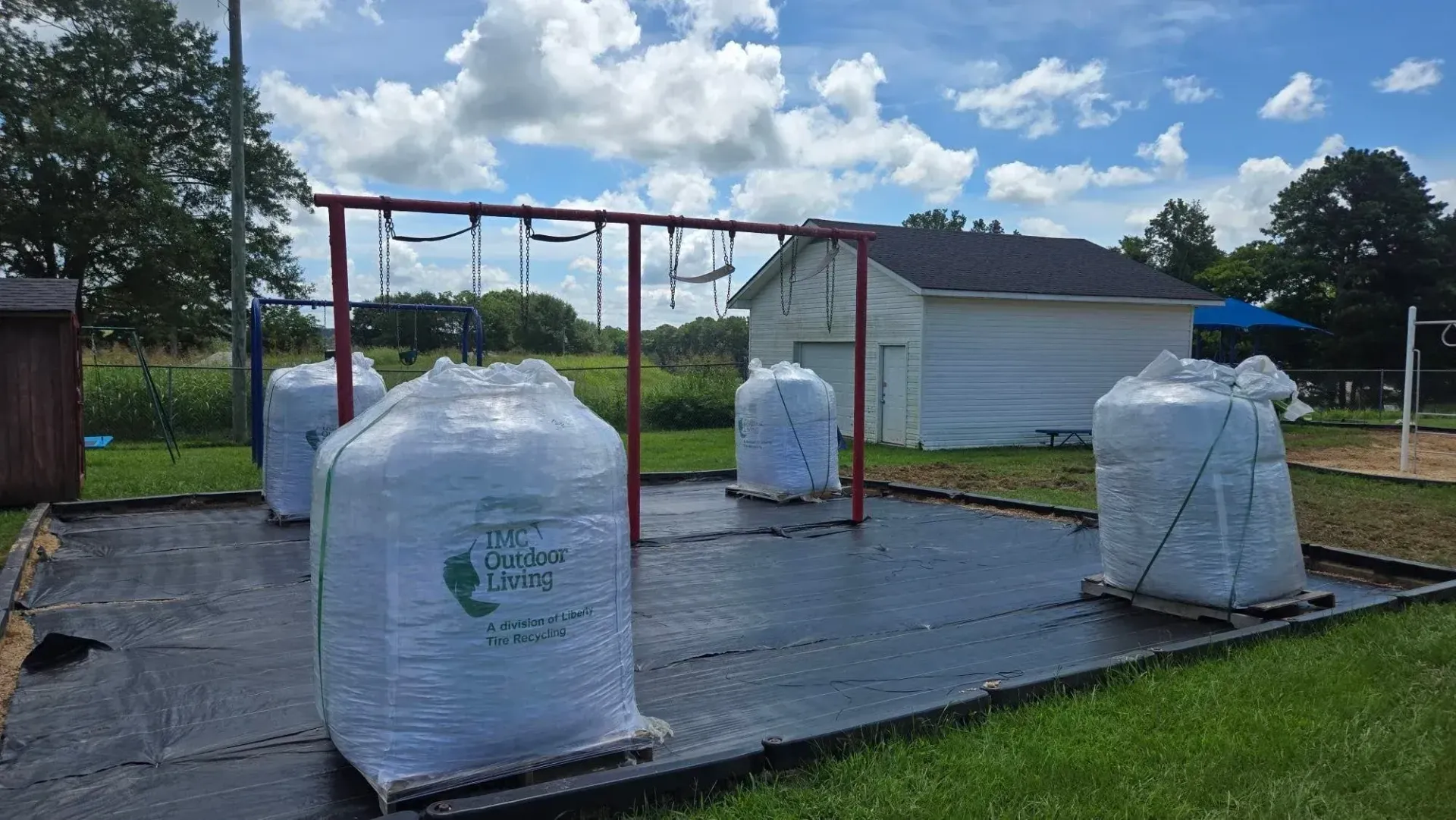 Outdoor playground with covered equipment wrapped in white protective sheeting and red climbing frames on wet pavement