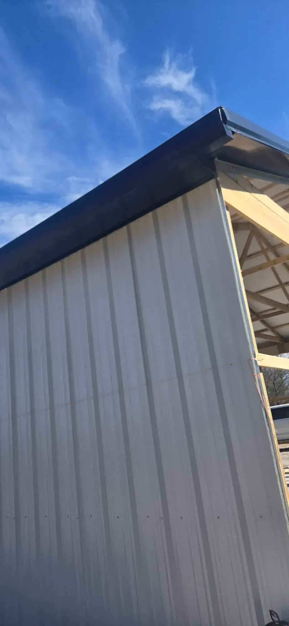 White corrugated metal building corner with dark roof against a blue sky