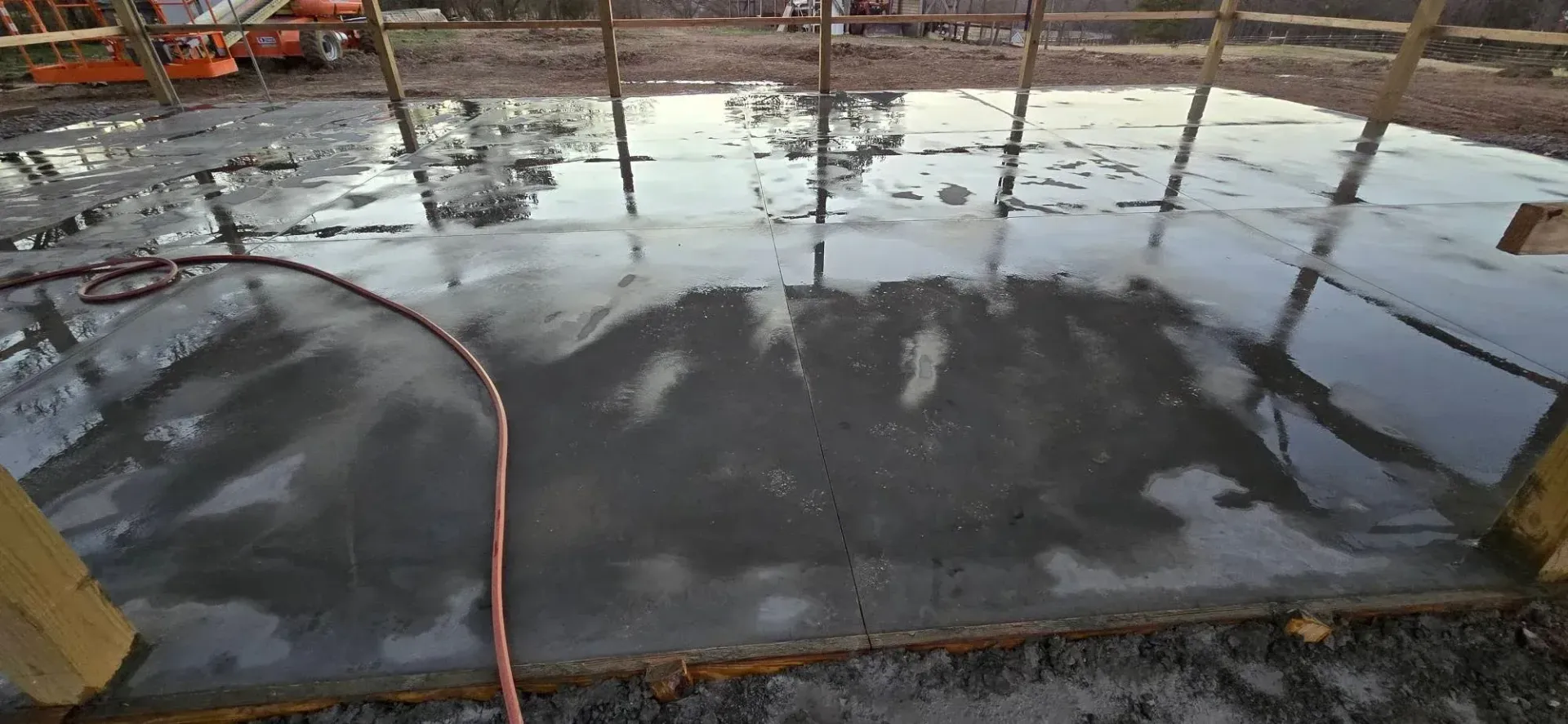 Freshly poured concrete slab reflecting trees and sky, with orange hose along the edge
