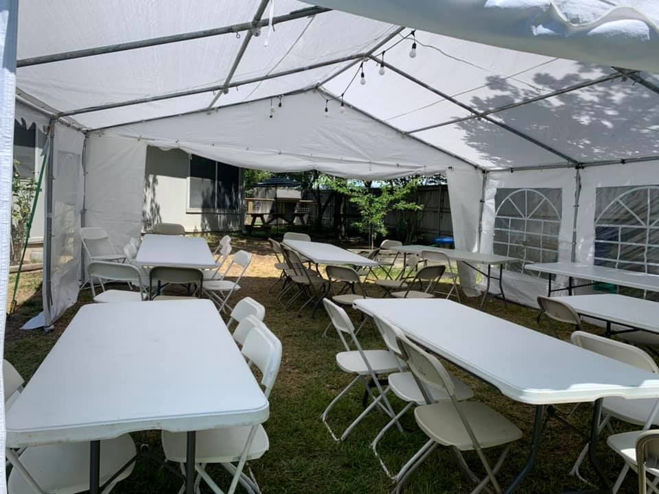 White event tent set up outdoors with multiple white rectangular tables and matching chairs arranged for a gathering.
