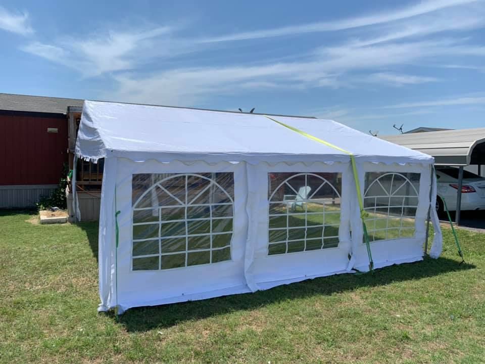 A white outdoor party tent with arched vinyl windows set up on a grassy lawn under a blue sky.