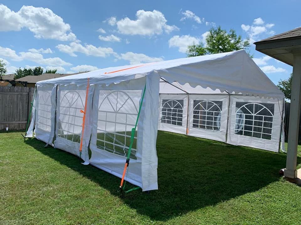 A large, rectangular white event tent with arched windows standing on a green grass lawn under a bright, cloudy sky.