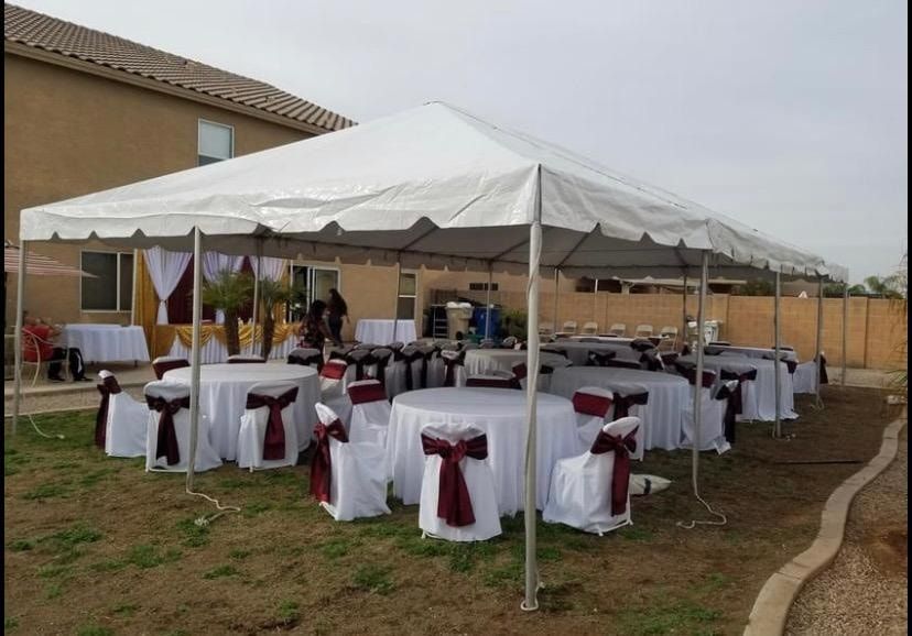 Outdoor event tent set up in a backyard with white-clothed round tables and chairs decorated with dark red sashes.