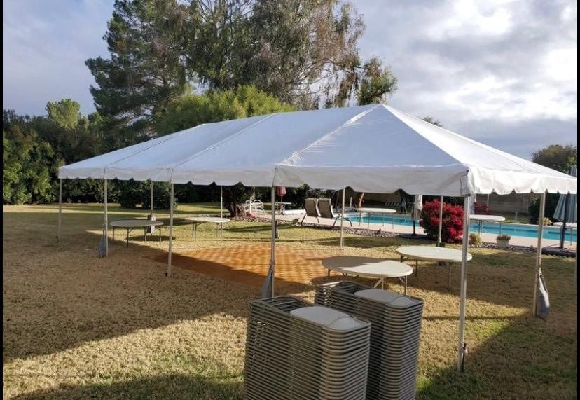 A large white event tent set up on a grassy lawn next to a swimming pool, with round tables and chairs visible.