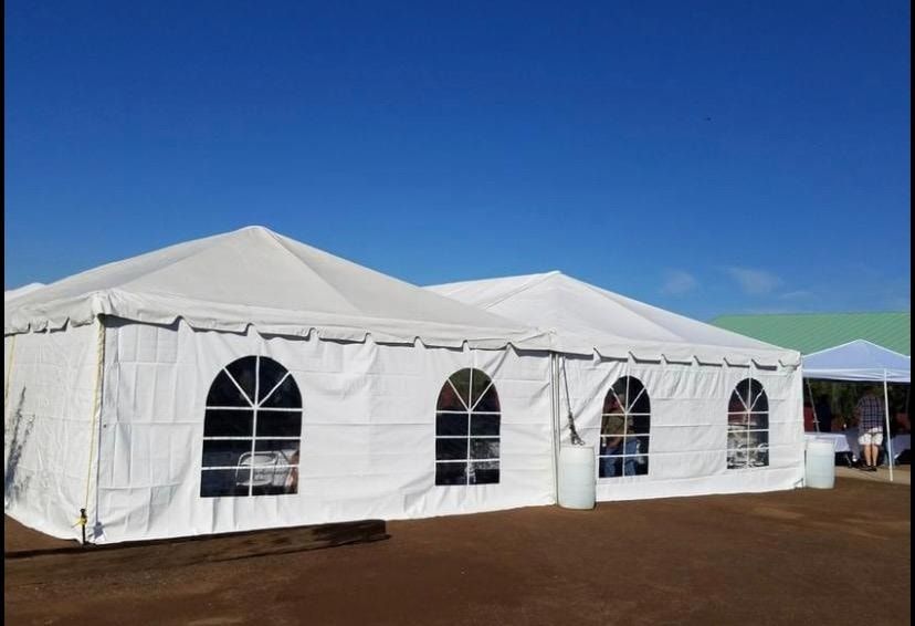 Large white frame tent with arched windows standing on dirt ground against a clear blue sky.