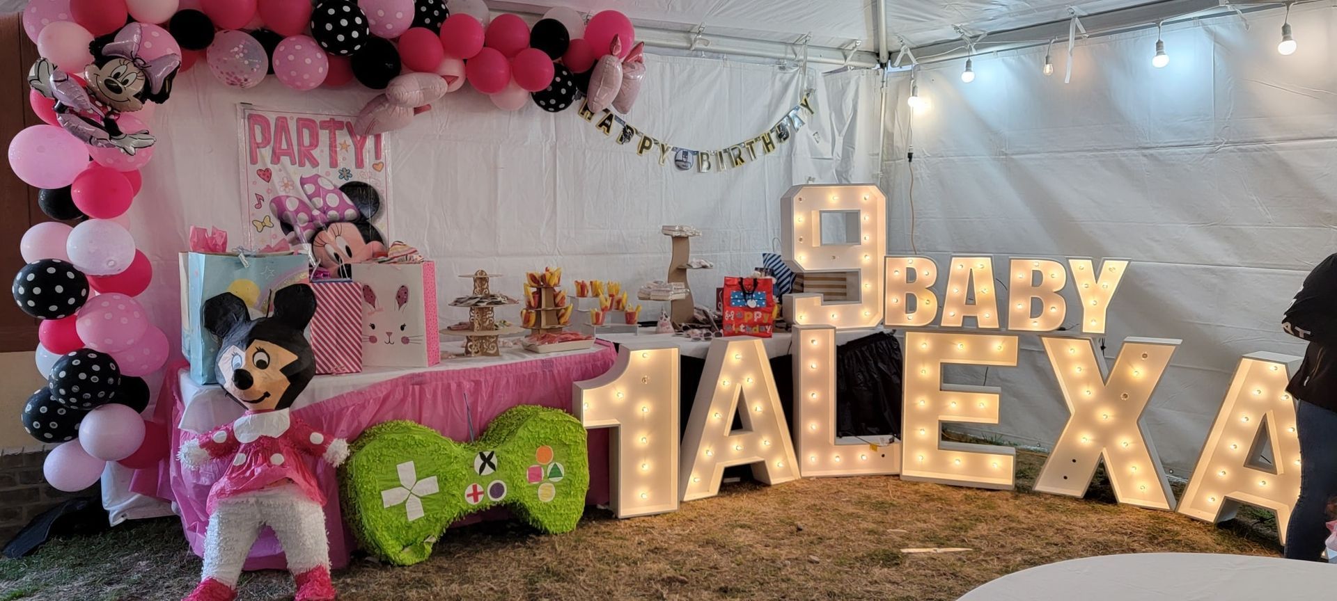 A Minnie Mouse-themed birthday display with balloons, a mascot figure, and glowing marquee letters spelling 