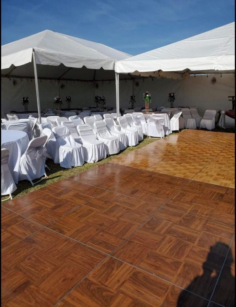 Outdoor wedding reception setup with white-covered chairs under tents beside a large wooden dance floor.