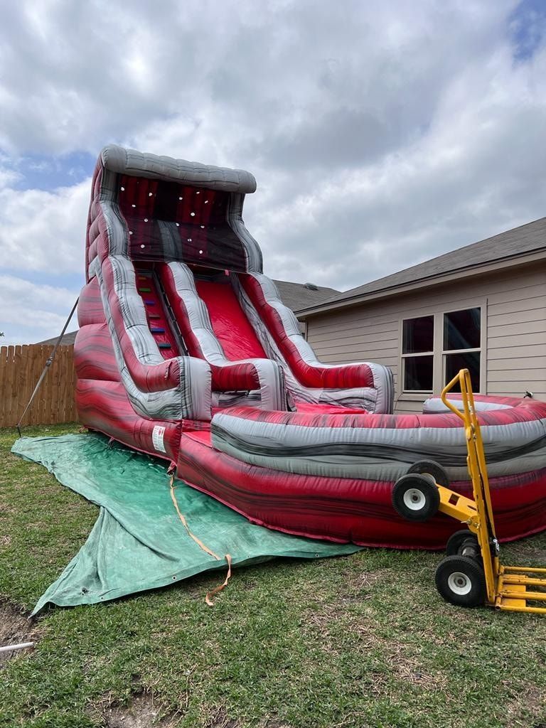 A large, red and gray inflatable water slide set up on a grassy lawn next to a yellow hand truck.