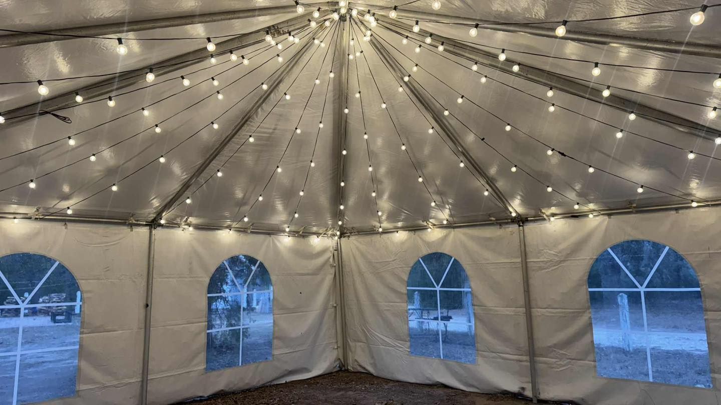 The interior of a white event tent decorated with strings of glowing lights radiating from the center to the edges.