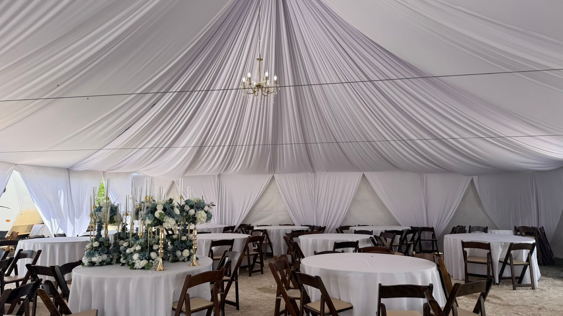 A white event tent with arched windows and orange tie-down straps stands on a green grass lawn under a blue sky.