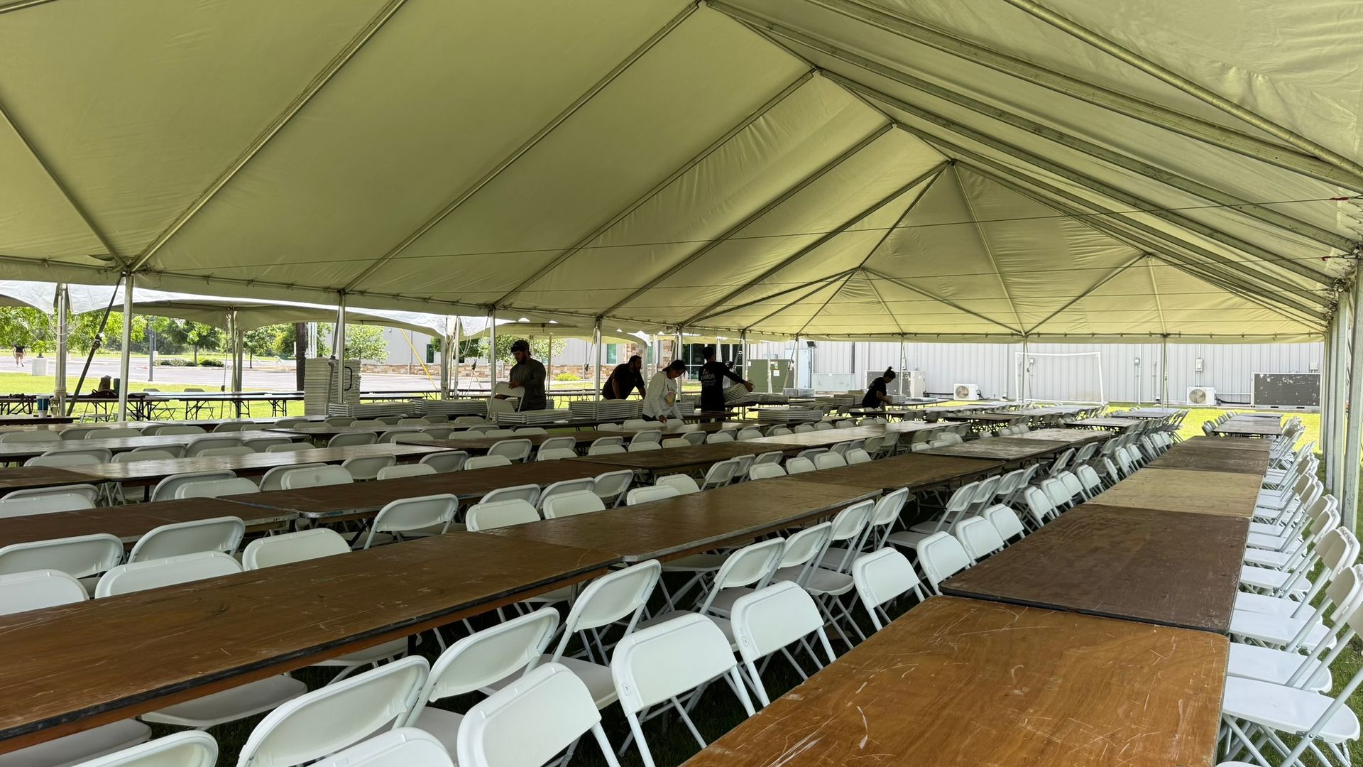 A large white event tent set up on a grassy lawn next to a swimming pool, with round tables and chairs visible.