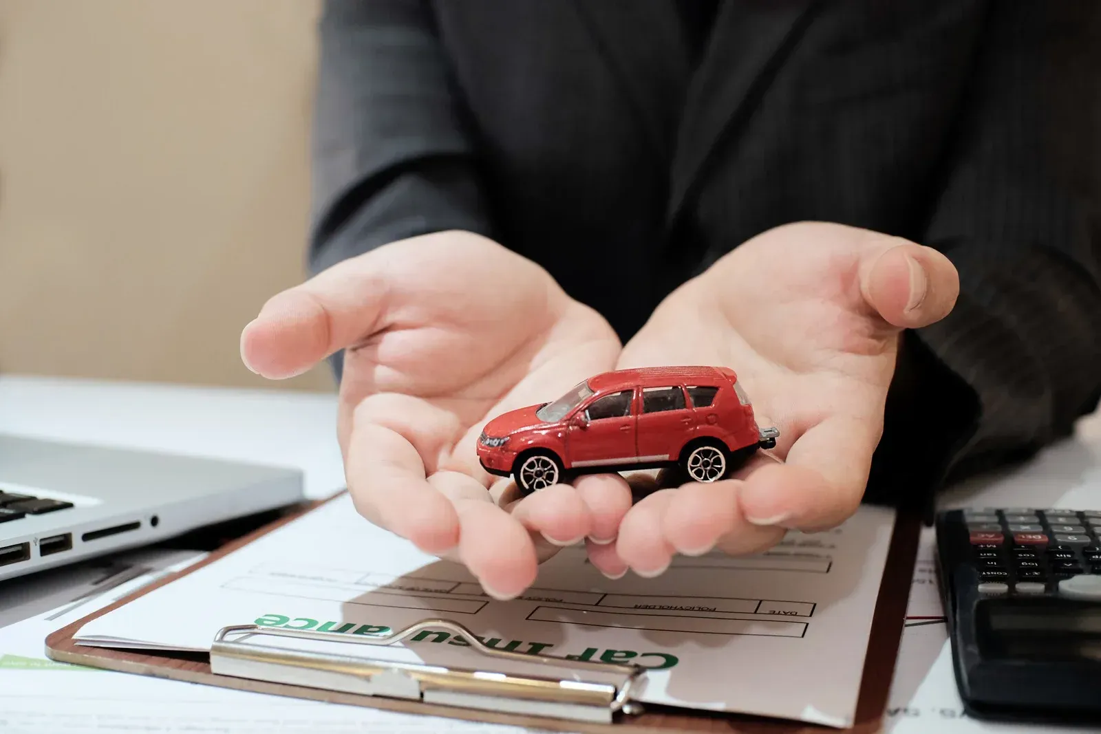 A person is holding a toy car in their hands over a clipboard.