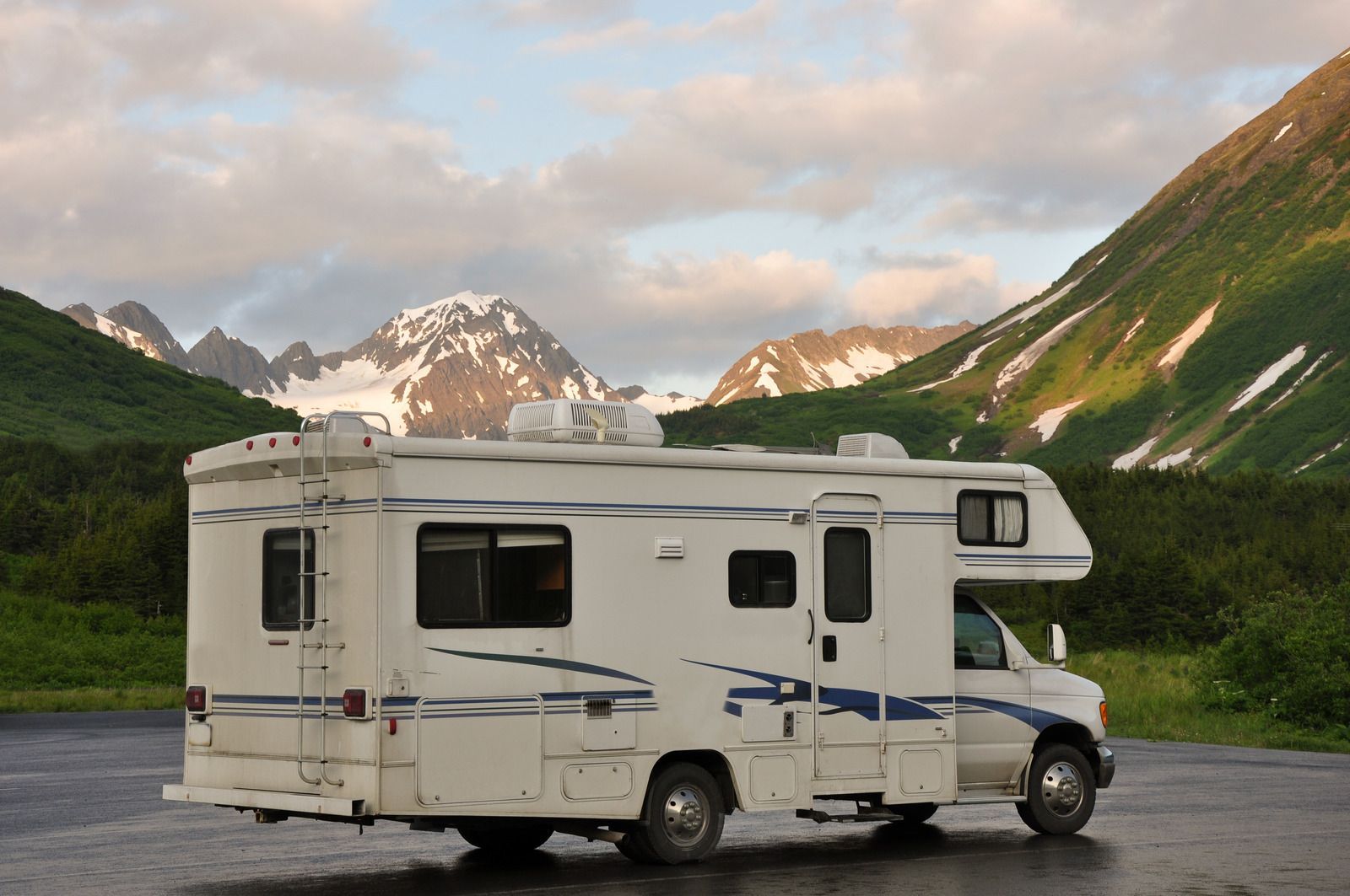 A white rv is parked in a parking lot with mountains in the background