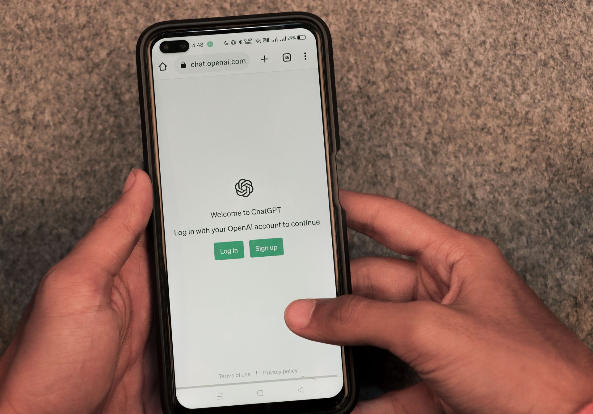 Hands holding a smartphone displaying a login screen with green buttons on a brown surface