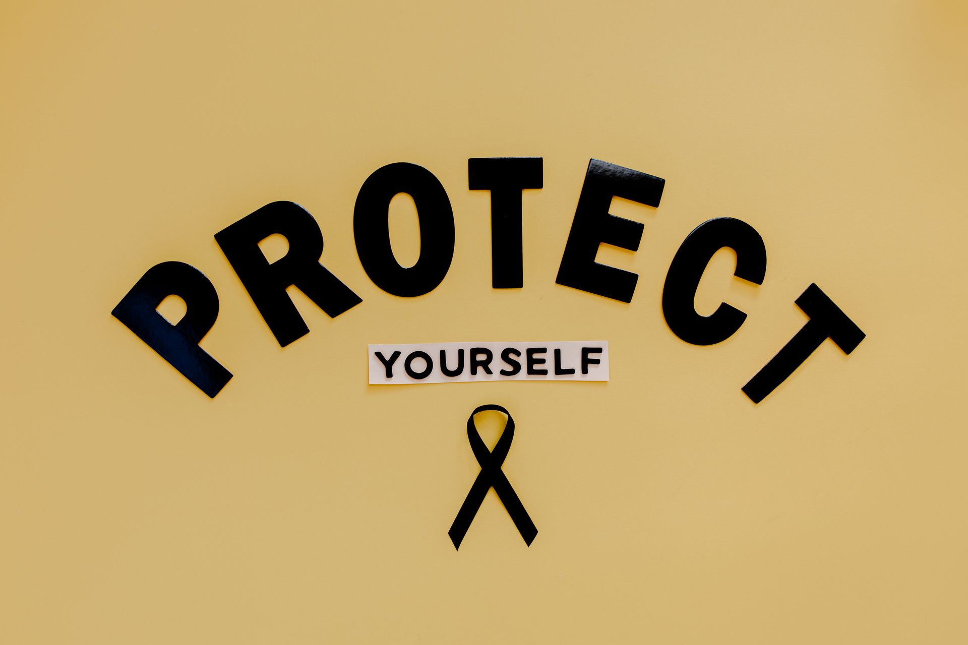 Black ribbon awareness graphic with “PROTECT YOURSELF” on a tan background