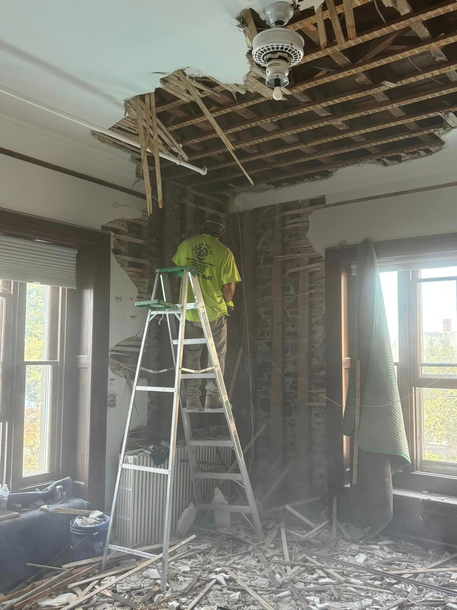 A man standing on a ladder in a room with a hole in the ceiling