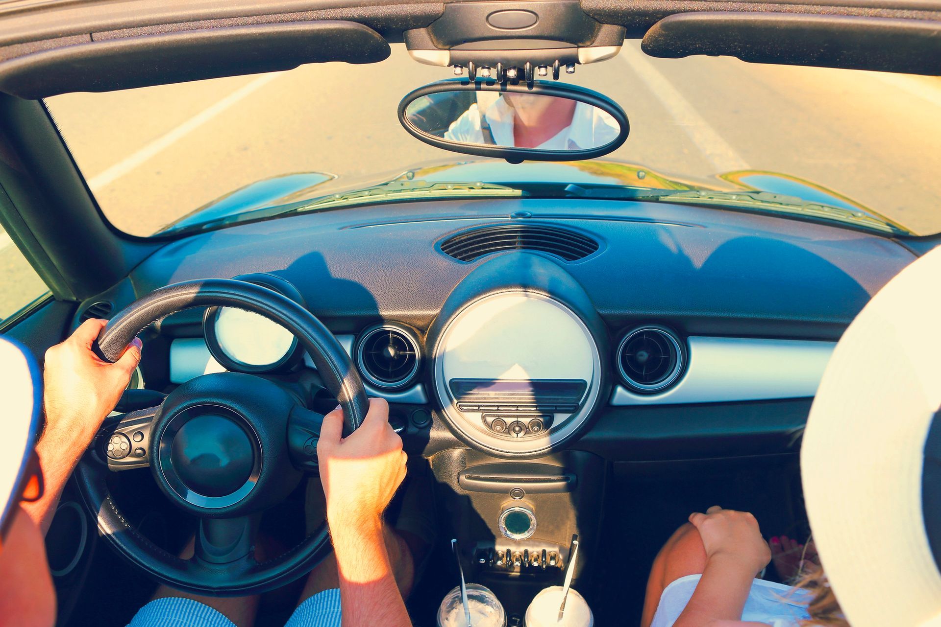 Vista dal punto di vista del guidatore dell'abitacolo di un'auto d'epoca, con volante, indicatori del cruscotto e strada visibile attraverso il parabrezza.