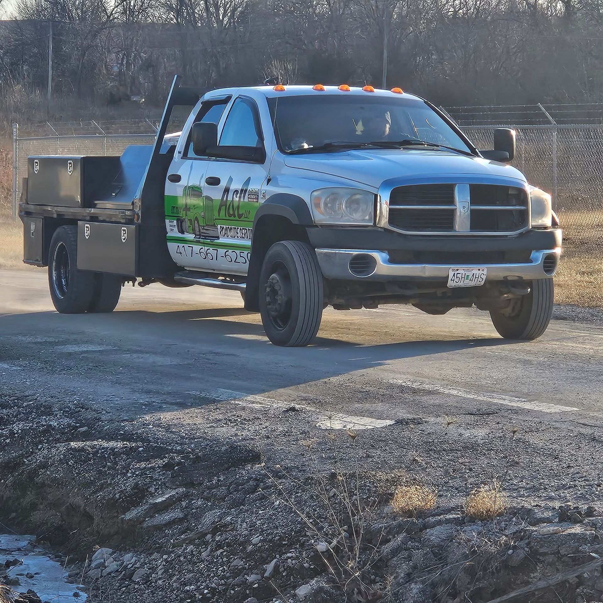 Silver pickup truck with green graphics driving on a gravel lot