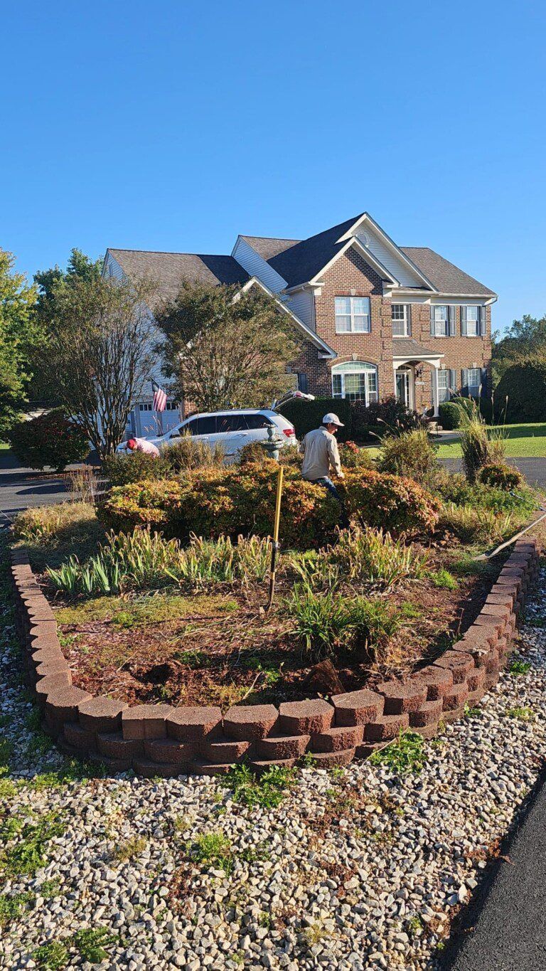 Person gardening in front yard with brick border. House and car in background.