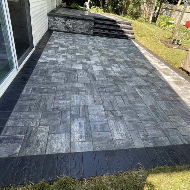 Paver patio with dark border and steps leading to grass. Gray and black tones dominate.