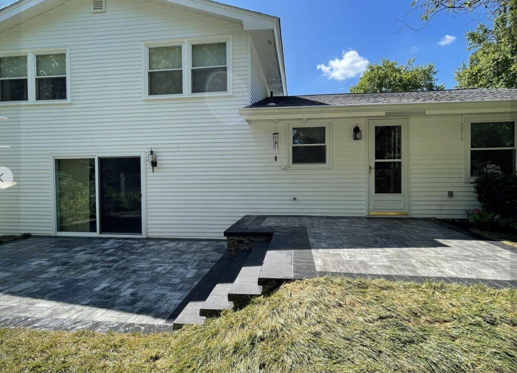 White house exterior with patio and steps leading to a yard with green grass.